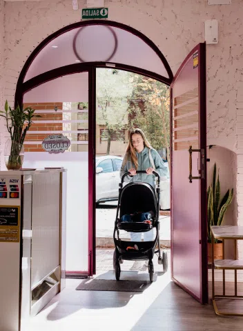 Madre entrando en el establecimiento con un carrito de bebé, mostrando un espacio iluminado, accesible y acogedor.