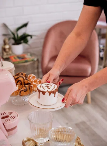Chocolate caliente con crema siendo servido sobre una mesa con cristalería, pasteles y detalles decorativos en tonos suaves.