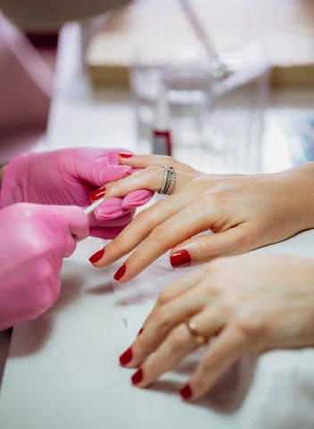 Primer plano de una manicura, con manos cuidadas y uñas pintadas de rojo intenso mientras la profesional aplica un toque final.