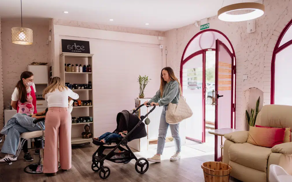 Madre entrando al espacio con un carrito de bebé, transmitiendo un ambiente cálido y accesible para familias. Al fondo, estanterías con productos de belleza y cuidado personal.