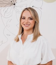 Mujer rubia de cabello liso y blusa blanca, sonriendo frente a un fondo decorado con líneas artísticas, proyectando profesionalismo y calidez.