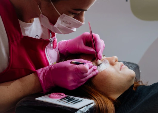 Profesional utilizando pinzas para aplicar extensiones de pestañas a una cliente, en un ambiente sereno con enfoque en precisión.