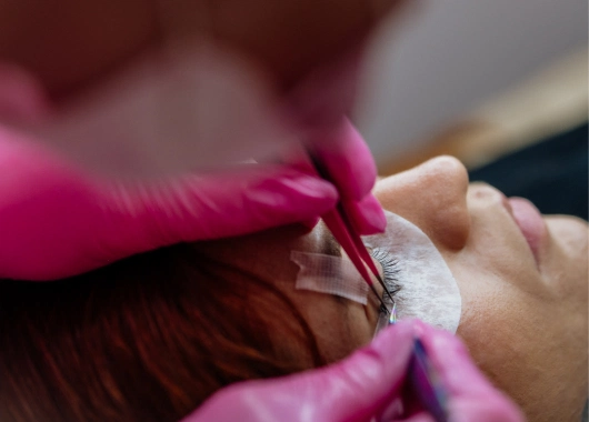 Primer plano de la aplicación de extensiones de pestañas, mostrando un trabajo detallado y delicado para realzar la mirada de la cliente.