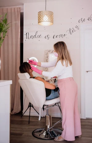 Profesional aplicando un tratamiento facial a una cliente en un sillón reclinable, en un ambiente acogedor con una frase motivadora en la pared que dice "Nadie es como tú".