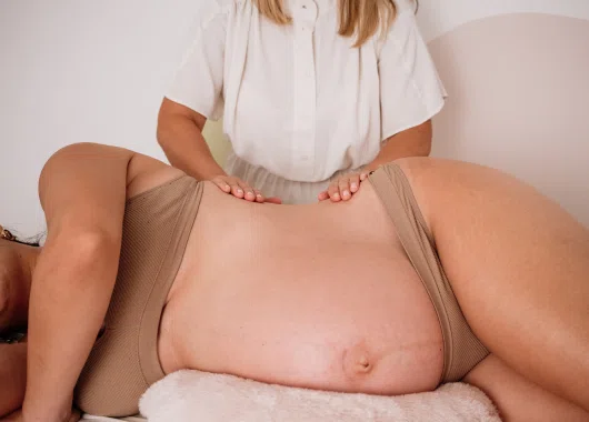 Mujer embarazada recibiendo un masaje en la espalda, acostada de lado, destacando el cuidado y bienestar durante el tratamiento.