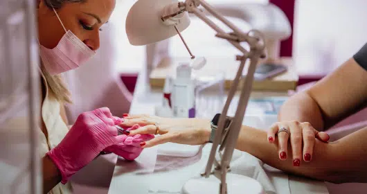 Profesional realizando una manicura con guantes rosas, destacando precisión y cuidado en un ambiente bien iluminado.