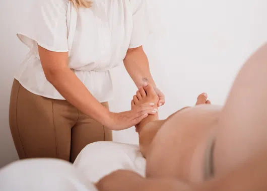 Profesional masajeando los pies de una mujer embarazada, brindando atención cuidadosa en un espacio tranquilo.