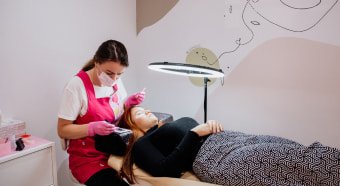 Profesional realizando un tratamiento de diseño de cejas a una cliente recostada, en un espacio tranquilo con iluminación enfocada y decoraciones minimalistas.