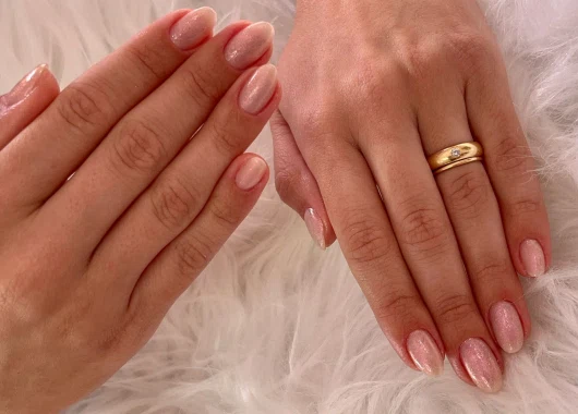 Cliente disfrutando de una manicura profesional en un ambiente moderno y acogedor, atendida por una especialista con guantes rosas.